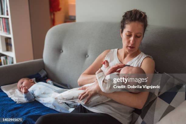 woman sitting by one baby boy on the bed and holding other one - parental leave stock pictures, royalty-free photos & images