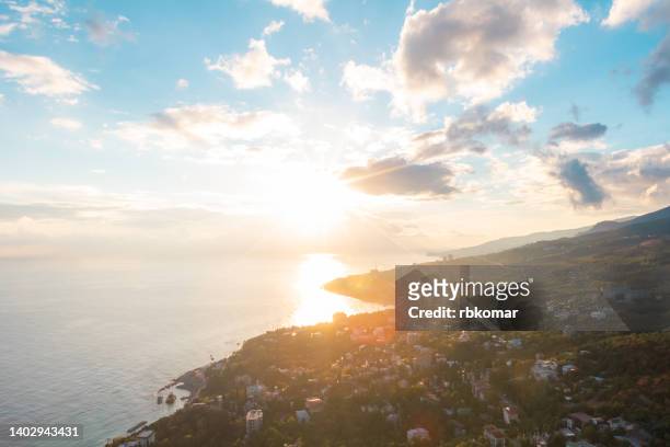 morning sunrise in a dramatic cloudy blue sky over a calm sea. bright rays of the sun shine on the coastal resort town and distant mountain silhouettes - ukraine landscape bildbanksfoton och bilder