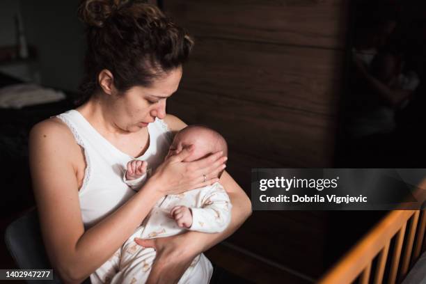 concerned woman holding crying newborn baby in her arms - new mother stock pictures, royalty-free photos & images