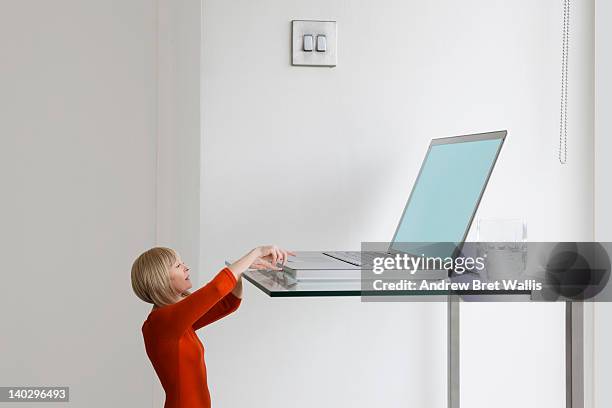 little businesswoman reaches for giant laptop - size foto e immagini stock