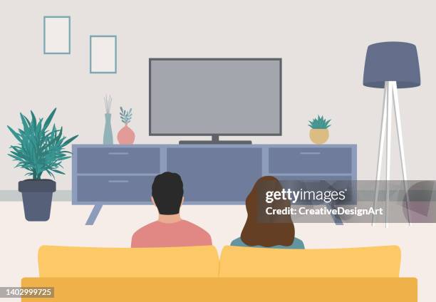 bildbanksillustrationer, clip art samt tecknat material och ikoner med rear view of young couple sitting on sofa and watching television - mysig