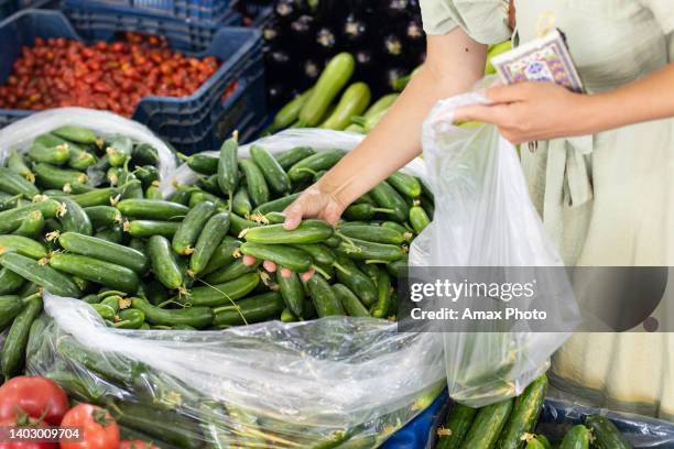 a woman at the street actual market chooses fresh organic fruits and vegetables - large cucumber stockfoto's en -beelden