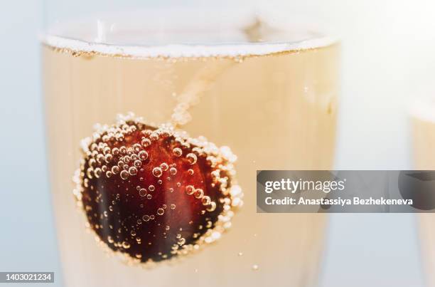 cherries covered with bubbles in glass of champagne under the sun - bulles champagne photos et images de collection