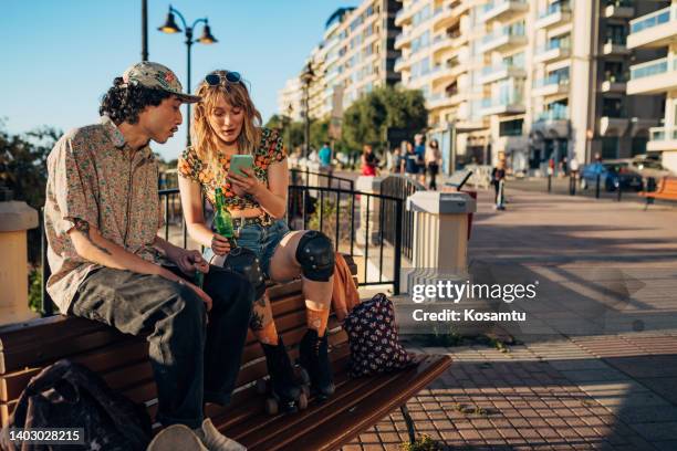 two best friends sitting on a bench in a public park and looking at something on smartphone - sea iphone stock pictures, royalty-free photos & images