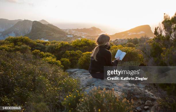 woman sitting on top of a hill, reading a book - solitude stockfoto's en -beelden