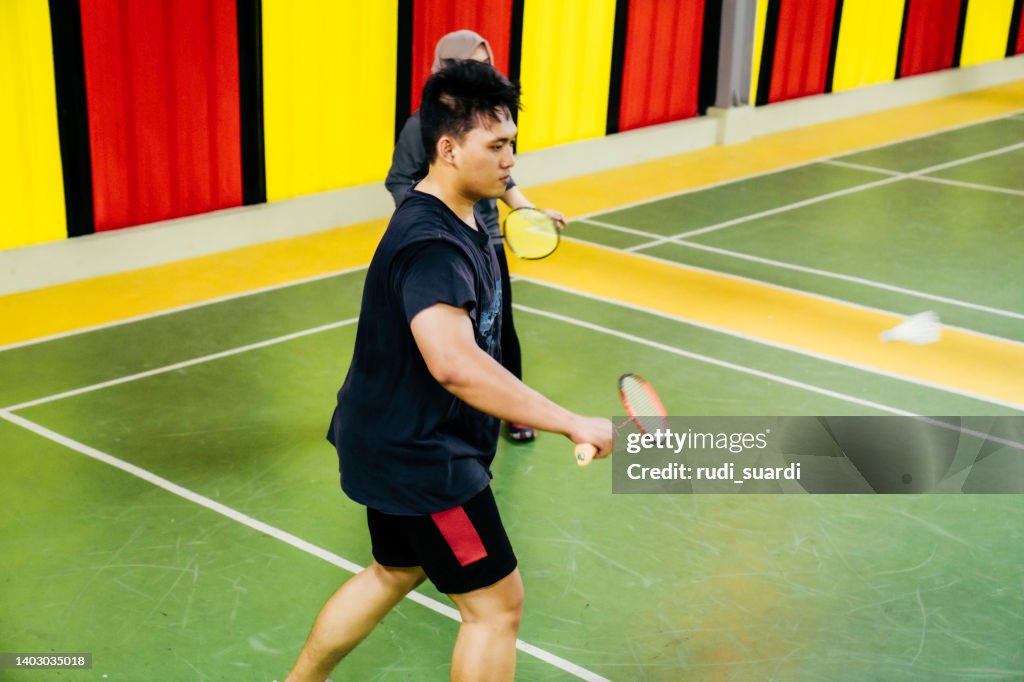 Two couples playing badminton against each other on an indoor court.