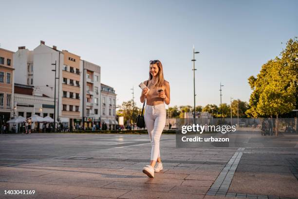 young woman with phone walking down the street - insulated drink container stock pictures, royalty-free photos & images