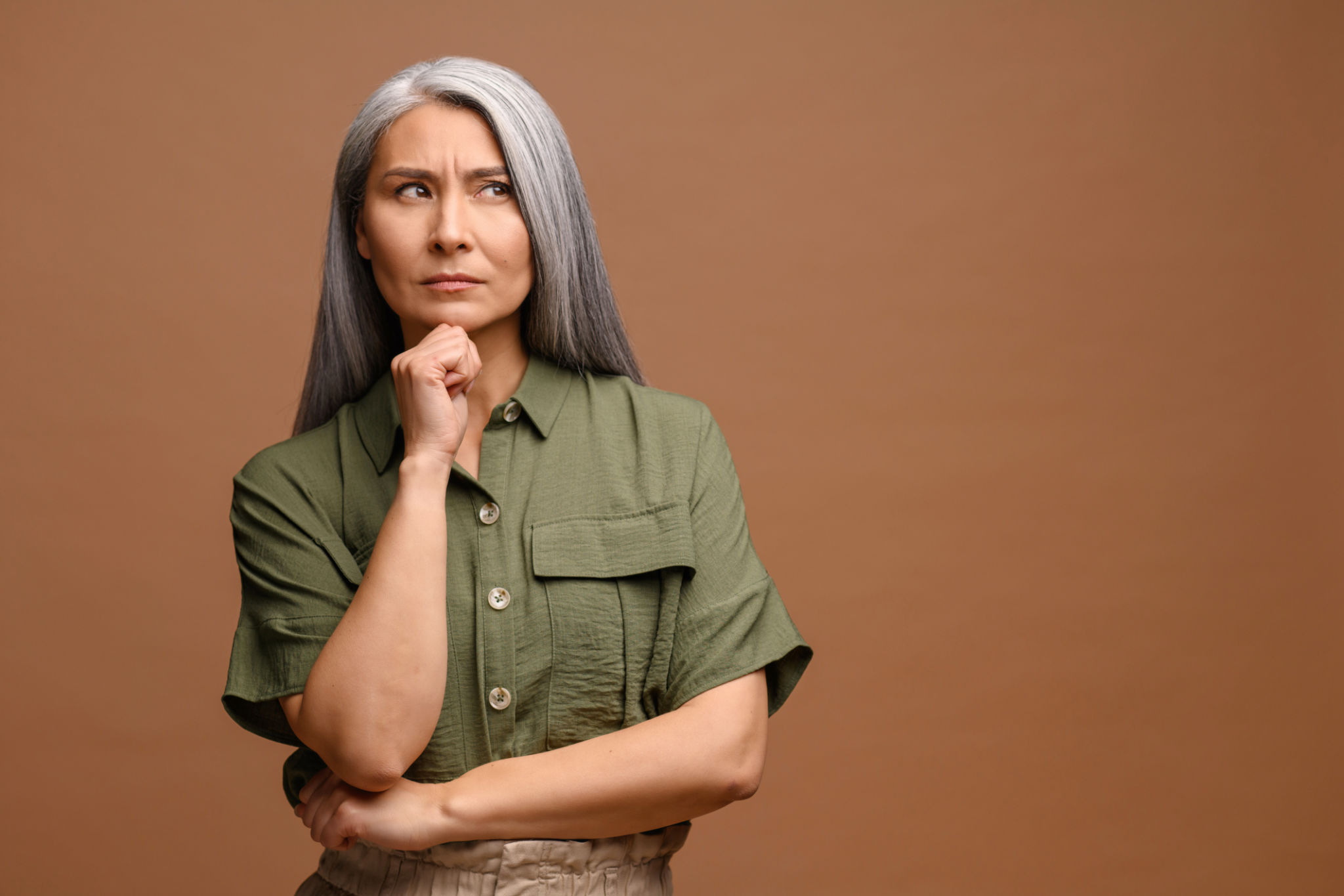 Smart and thoughtful mature woman holding her chin and pondering idea, making difficult decision, looking uncertain doubtful. Indoor studio shot isolated on beige Smart and thoughtful mature woman holding her chin and pondering idea, making difficult decision, looking uncertain doubtful. Indoor studio shot isolated on beige
