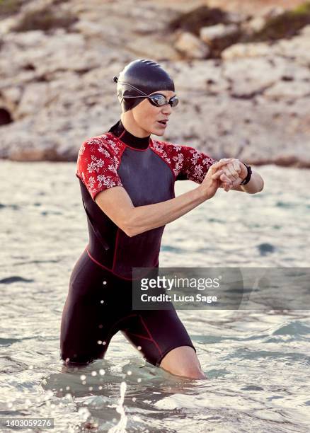 a swimmer checks her fitness tracker watch as she leaves the mediterranean sea - early termination bildbanksfoton och bilder