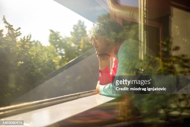 caucasian teenage boy with curly half dyed blue hair looking through window - sun rays through window stock pictures, royalty-free photos & images