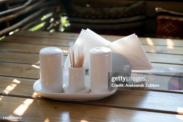 beautiful white ceramic salt and pepper shakers on a wooden table, in a cafe, restaurant or home kitchen, outdoors. seasonings and spices to add to food. nearby are napkins in a stand or napkin holders. - 胡椒入れ ストックフォトと画像