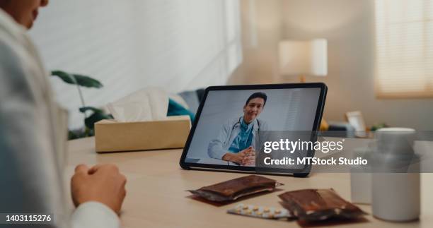 close up of sick young asian woman using tablet talk to doctor in living room at home. - telehealth visit stock pictures, royalty-free photos & images