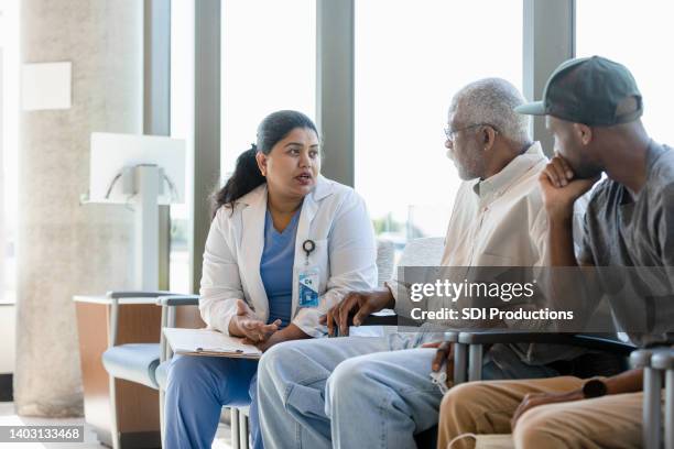 senior man and his son listen to female doctor - family with doctor stock pictures, royalty-free photos & images