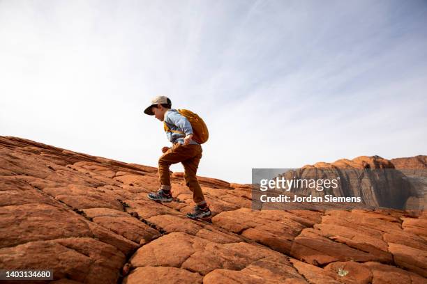 a young boy hiking up a rocky hill in the desert. - st george utah 個照片及圖片檔