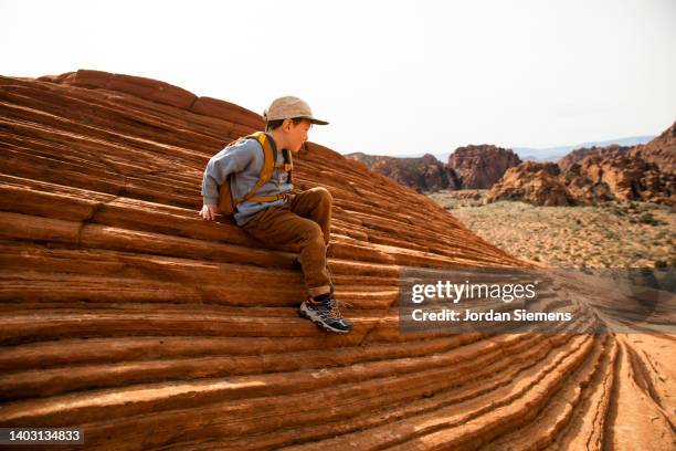 a young boy sitting on a unique rock formation while hiking in the desert. - geology class stock pictures, royalty-free photos & images