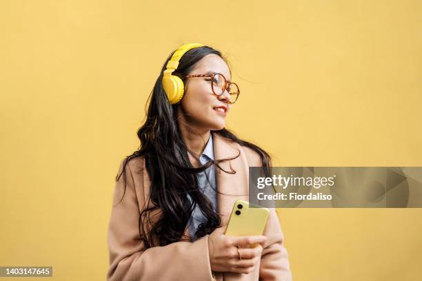 young asian woman in coat with yellow headphones - vietnam spring stock pictures, royalty-free photos & images