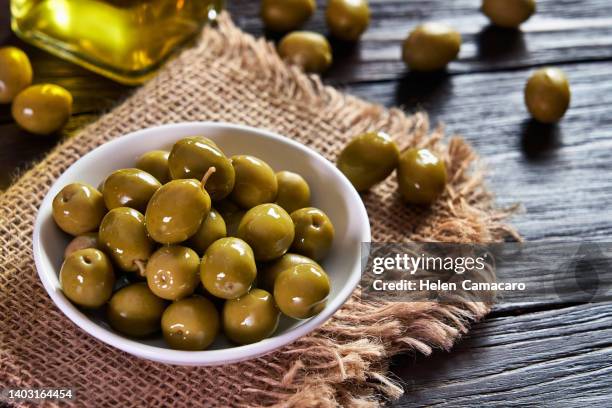 bowl filled with green olives on rustic wooden table - olive fotografías e imágenes de stock