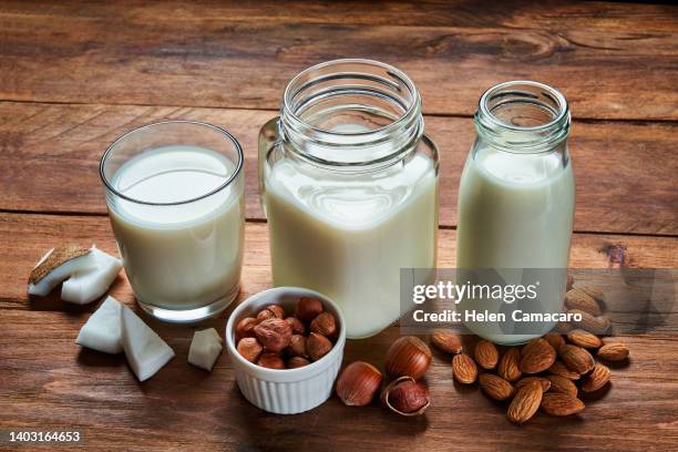 alternative types of vegan milks in glass bottles on rustic wooden table - replaces stock-fotos und bilder