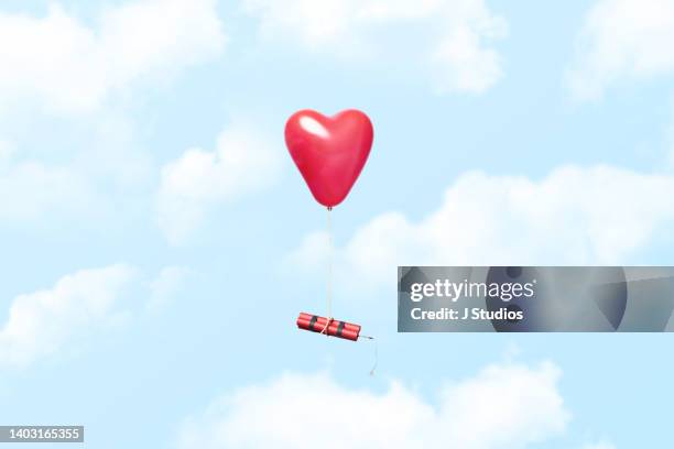 heart shaped balloon carrying a dynamite stick - menselijke relaties stockfoto's en -beelden