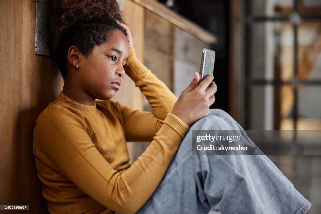 Bored black girl using cell phone while relaxing at home.