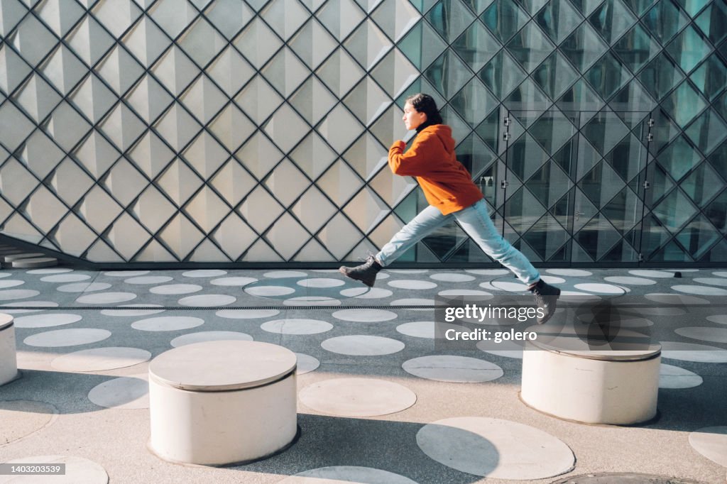 Woman jumping from bench to bench on white spotted town square