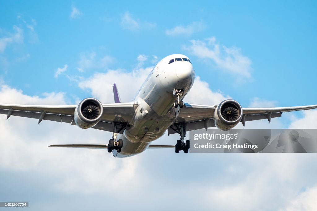 Front view of white 777 commercial flight airplane taking off or landing from the Airport runway with no visible markings or livery. Blue sky sunny back drop with some clouds