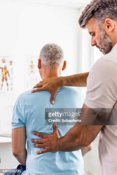male doctor and patient suffering from back pain during medical exam - looking over shoulder stockfoto's en -beelden