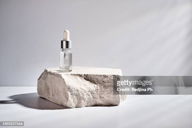 cosmetic vial with transparent cosmetic gel serum texture stands on rock podium with hard shadow. beauty concept of cosmetic products for moisturising and whitening the skin. - rock object stock pictures, royalty-free photos & images
