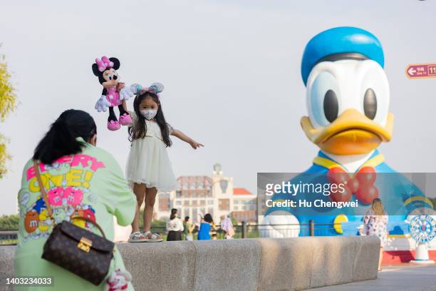 Girl poses for photo with Mickey Mouse doll in Disneytown on June 16, 2022 in Shanghai, China. Disneytown and the Shanghai Disneyland Hotel have...