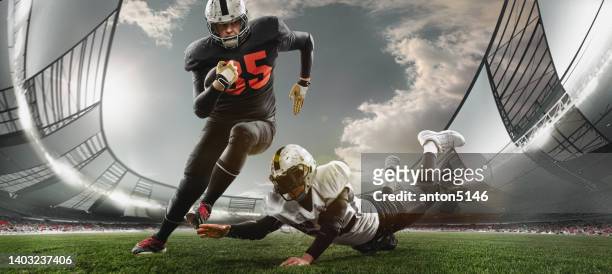 two american football players in action, motion. sportsmen fight for ball during game at crowded stadium at evening time - footballs stockfoto's en -beelden