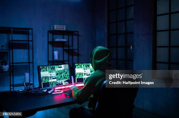 hacker man working on computers in dark room, rear view. - computer hacking stock-fotos und bilder
