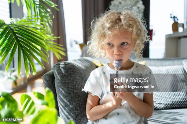 toddler girl licking a yoghurt covered spoon - yogurt spoon stock-fotos und bilder
