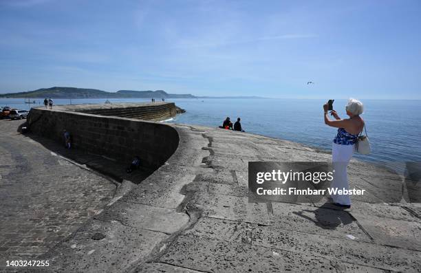 Woman takes a photo o The Cobb, on June 16, 2022 in Lyme Regis, England. Hot air originating in North Africa and travelling up through Spain brings...