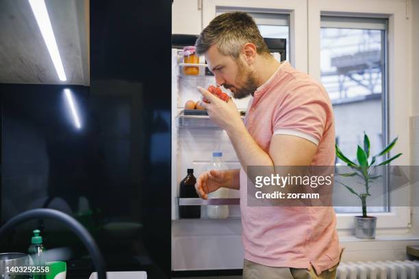 man standing in the kitchen, holding a box of cherry tomatoes and smelling it - suspicious package stock pictures, royalty-free photos & images