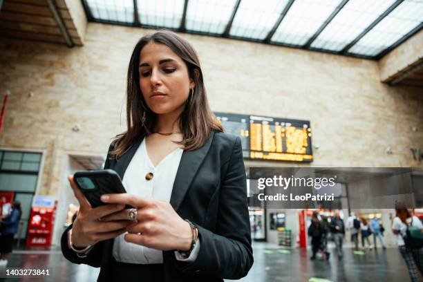 a woman is checking messages on mobile phone while waiting at the railway station - female worried mobile imagens e fotografias de stock