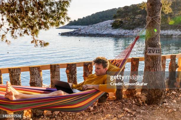 homem trabalhando em laptop em rede enquanto acampava ao lado do mar - hvar - fotografias e filmes do acervo