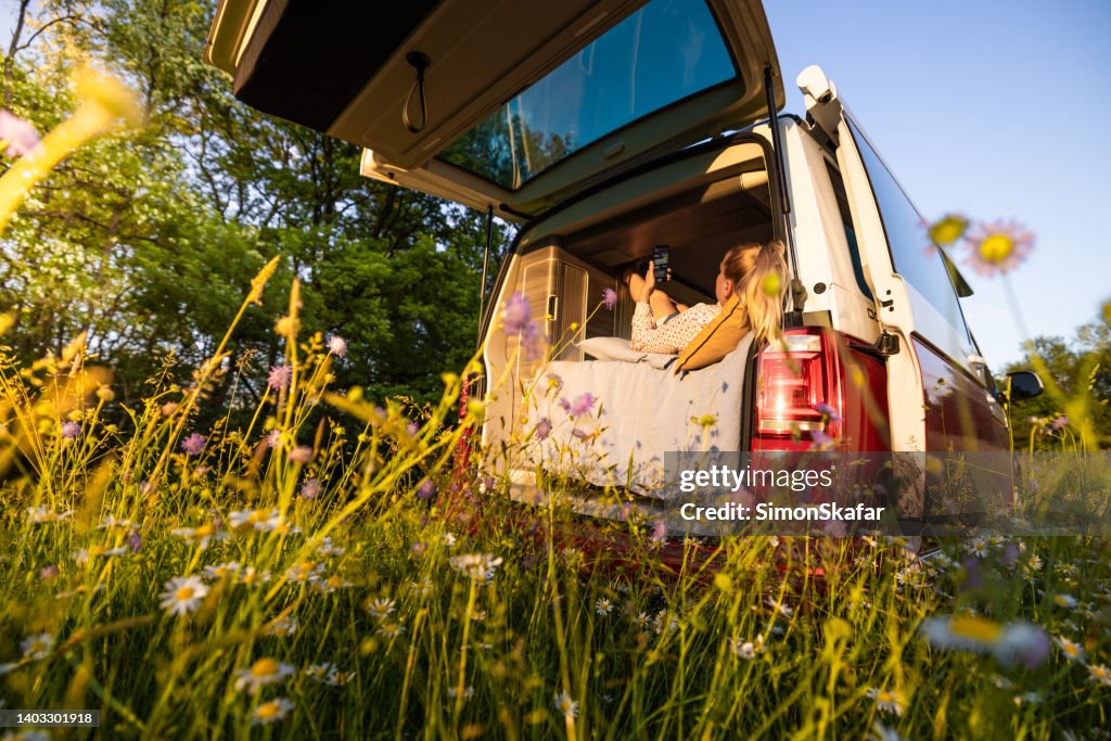 Mujer acostada en la cama mientras usa el teléfono móvil dentro de la camioneta