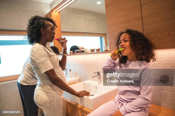 black pregnant woman and cute daughter brushing their teeth at home - adult in mirror stock pictures, royalty-free photos & images