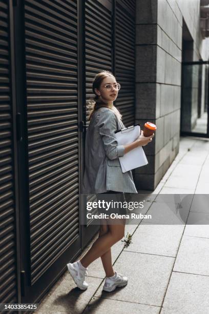 young woman with papers and cup against closed shutters. - skirt suit stock-fotos und bilder