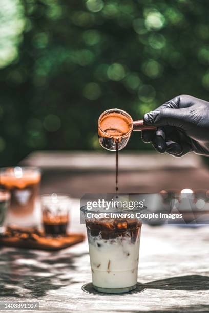 closeup barista hands pouring espresso shot to cup of ice and milk - iced coffee foto e immagini stock