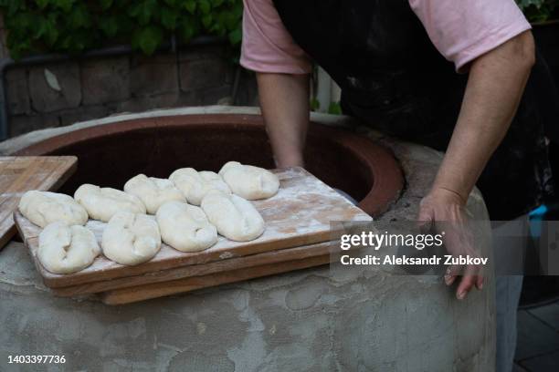 a georgian woman baker bakes tortillas in a tandoor, outdoors. the process of cooking and baking bread in a traditional georgian oven - tone, tandoor. home national bakery. women's duties, home life. - lavash stock-fotos und bilder