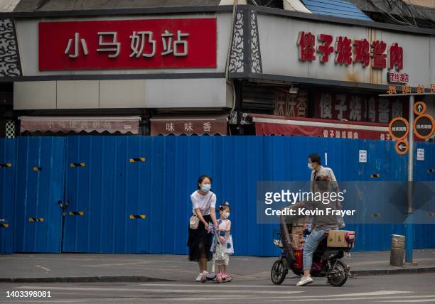 Woman and her child wear masks as they cross an intersection in front of a fenced off business area that has been locked down due to a COVID-19...