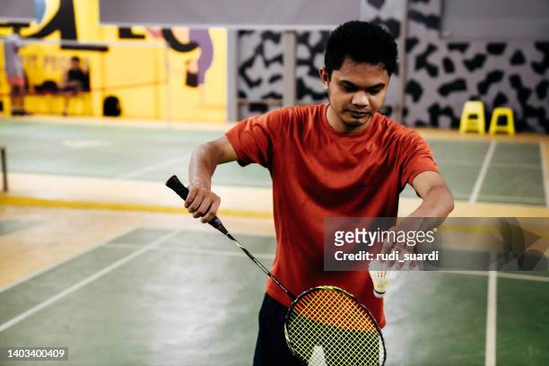 mid adult man hitting shuttlecock with badminton racquet in court. - badminton stock pictures, royalty-free photos & images