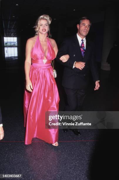 American glamour model and actress Anna Nicole Smith , wearing a pink halter neck evening gown, accompanied by a man, attends the Video Software...