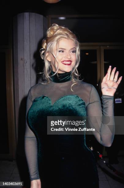 American glamour model and actress Anna Nicole Smith , wearing a dark green velvet evening gown with a sweetheart neckline and tulle sleeves, attends...