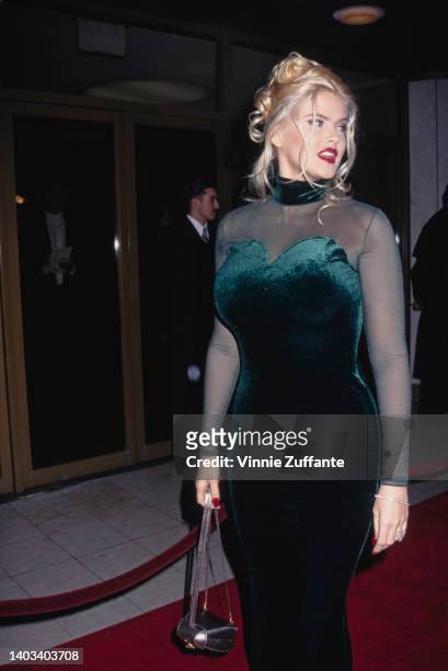 American glamour model and actress Anna Nicole Smith , wearing a dark green velvet evening gown with a sweetheart neckline and tulle sleeves, attends...