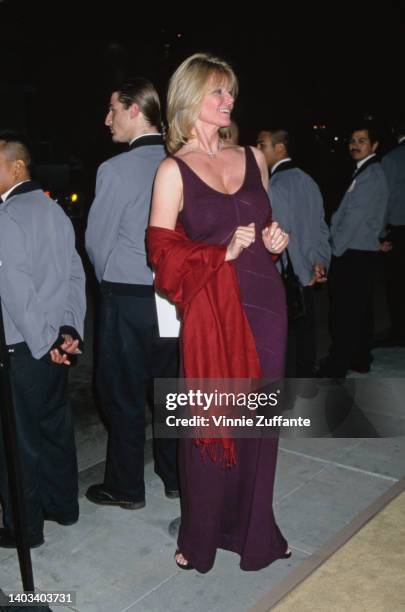 American fashion model Cheryl Tiegs, wearing a burgundy evening dress with a scoop neckline, with a red shawl draped over her arms, attends the 2nd...