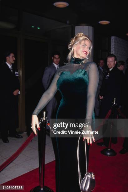 American glamour model and actress Anna Nicole Smith , wearing a dark green velvet evening gown with a sweetheart neckline and tulle sleeves, attends...