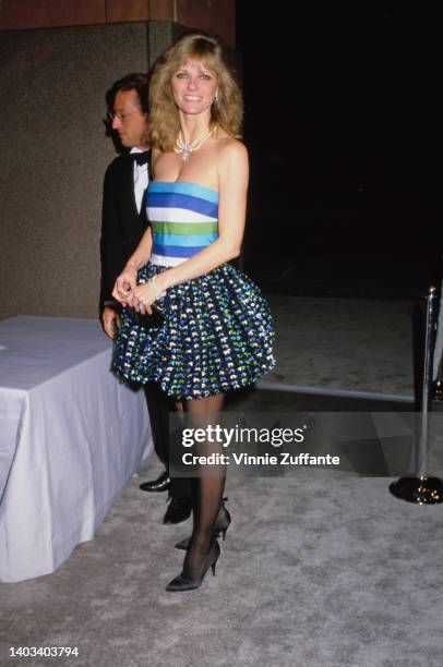 American fashion model Cheryl Tiegs, wearing a blue, green and white striped tube top and a blue, green and white spotted miniskirt, attends the...