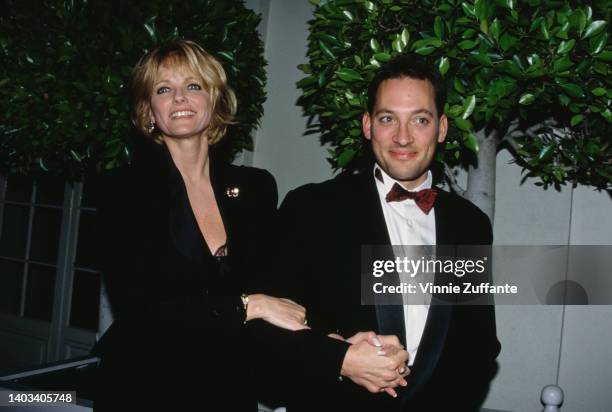 American fashion model Cheryl Tiegs, wearing a black suit, and her husband, American actor Anthony Peck, wearing a tuxedo with a deep red bow tie,...